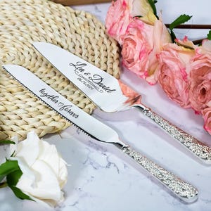May include: A silver cake knife and server set with ornate, textured handles. The knife is engraved with the text together forever, and the server is engraved with the names Lea & Daniel and the date 06.24.2024 in a cursive script font.