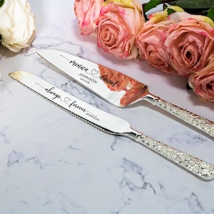 May include: A silver cake knife and server set with textured handles. The knife is engraved with "always forever JOHNSON" and the server features the names "Monica & Daniel", the surname "JOHNSON", and the date "04 15 22" in black script lettering.
