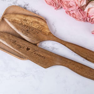 Puede incluir: Un juego de dos servidores de pastel de madera con texto grabado. El servidor más grande dice "Mr. & Mrs. JOHNSON Est. 2023" y el servidor más pequeño dice "Always Forever".