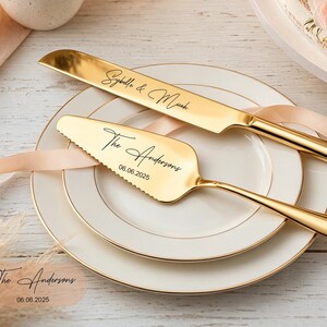 Puede incluir: Un juego de cuchillo y pala para pastel en tono dorado con grabado personalizado. El cuchillo tiene la inscripci&oacute;n Sybelle & Micah, mientras que la pala muestra The Andersons y la fecha 06.06.2025. Ambas piezas tienen un acabado met&aacute;lico pulido.