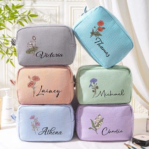 May include: Six striped cosmetic bags in various colors, stacked. Each bag features a floral embroidery and a name: Victoria, Thomas, Lainey, Michael, Athena, and Charlie. The bags are rectangular with a zipper closure.