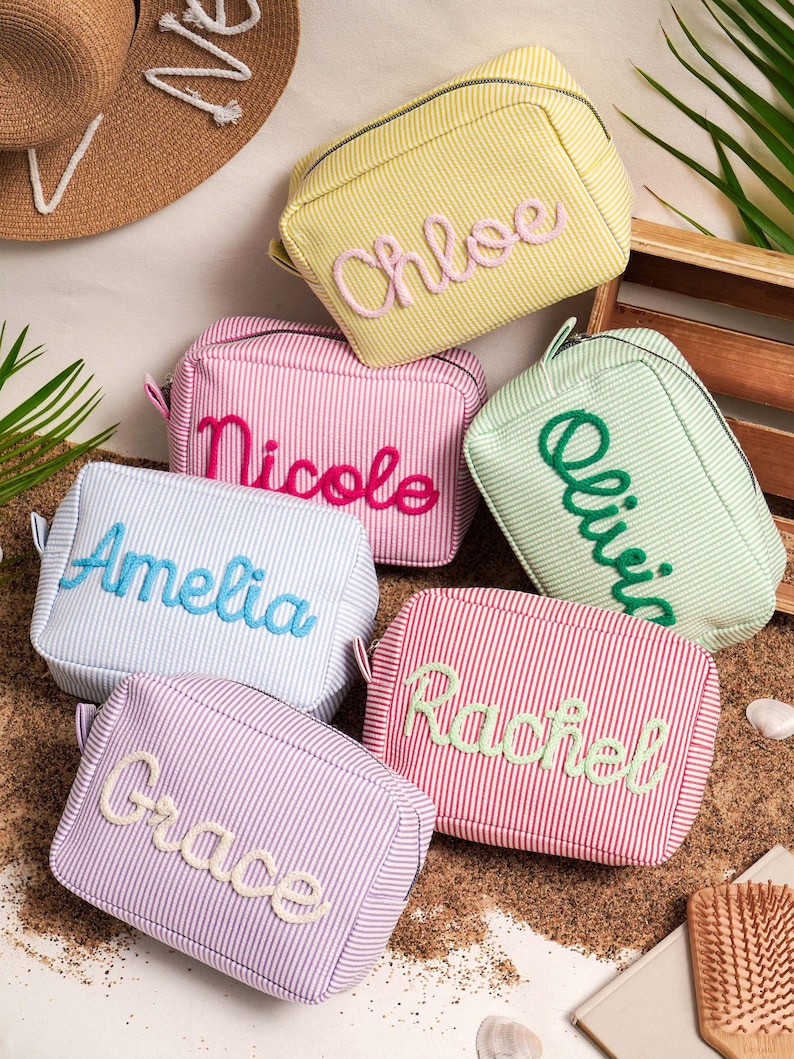 May include: Six rectangular zippered pouches in various pastel striped colors, each featuring a personalized name embroidered in a contrasting color. The names include Chloe, Nicole, Olivia, Amelia, Rachel, and Grace, displayed in a cursive font.