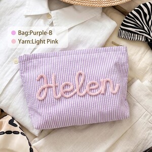 May include: A rectangular purple and white seersucker zippered pouch featuring the name Helen in raised light pink yarn lettering. The text on the overlay reads Bag:Purple-B and Yarn:Light Pink. The pouch is positioned on a white shirt.
