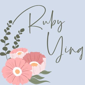 Op de afbeelding: Een lichtblauwe achtergrond met de naam "Ruby Ying" in cursief schrift. De naam wordt omringd door een bloemstuk van roze bloemen en groene bladeren.
