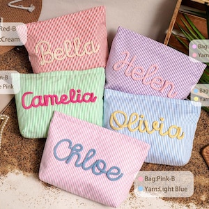 May include: Five rectangular zippered pouches with vertical stripes in red, green, purple, light blue, and pink. Each pouch features a name embroidered in raised yarn: Bella in cream, Camelia in rose pink, Helen in light pink, Olivia in yellow, and Chloe in light blue.