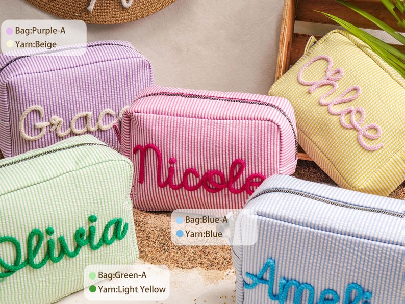May include: Five rectangular zippered pouches in pastel striped fabric, each featuring a name embroidered in raised yarn. The bags are purple with beige text, pink with dark pink text, yellow with pink text, green with green text, and blue with blue text.