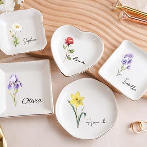 Op de afbeelding: Een witte keramische mok met een zwarte handgreep en de tekst "But First, Coffee" in een vetgedrukte, zwarte letter. De mok staat tegen een vage achtergrond. De mok is ongeveer 10 cm hoog.