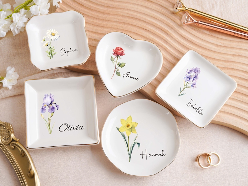Op de afbeelding: Een witte keramische mok met een zwarte handgreep en de tekst "But First, Coffee" in een vetgedrukte, zwarte letter. De mok staat tegen een vage achtergrond. De mok is ongeveer 10 cm hoog.