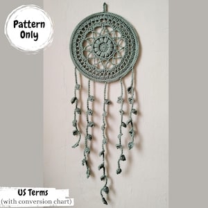 May include: A crochet dreamcatcher pattern in US terms with a conversion chart. The dreamcatcher is made of a light green yarn and features a circular design with a starburst pattern in the centre.
