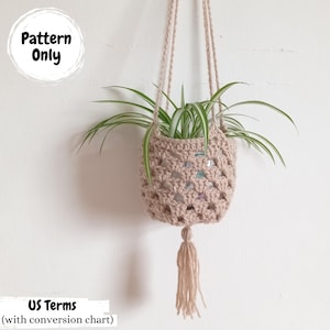 May include: A beige crochet plant hanger with a tassel, holding a green plant with long, slender leaves. The plant hanger is suspended from a beige cord. The text "Pattern Only" is in a white circle.