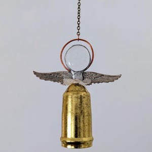 May include: A handcrafted angel ornament with a gold-colored base, silver wings, and a clear glass orb head. The angel is suspended by a chain and features a copper-colored halo. The wings are detailed and add a delicate touch to the design.