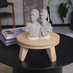 May include: A white ceramic mug with a black handle and the text "But First, Coffee" in a black, handwritten-style font. The mug is sitting on a wooden surface.