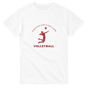 Pode incluir: Camiseta branca com uma silhueta vermelha de um jogador de voleibol a sacar a bola. O texto "Everything else is just a game" está em um círculo ao redor do jogador e a palavra "Volleyball" está abaixo do jogador.