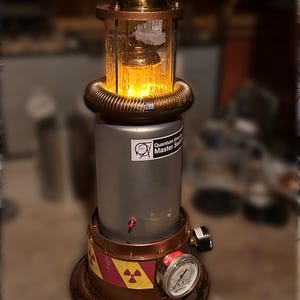 May include: A cylindrical lamp with a brass top, a glass chamber containing glowing yellow lights, and a grey body labeled Quantum time Master Switch. The base features a red and yellow radiation warning stripe and a circular pressure gauge.