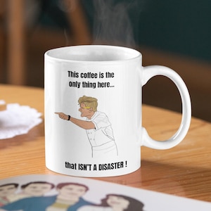 May include: White ceramic coffee mug with a black handle. The mug features a cartoon illustration of a chef pointing, with the text "This coffee is the only thing here... that ISN'T A DISASTER!" printed on the front.