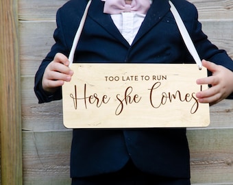 May include: A wooden sign with the text "Too Late To Run - Here She Comes!" in brown lettering. The sign is held by a child wearing a navy blue suit and a white bow tie.