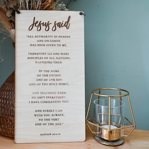 Könnte beinhalten: Ein Holzschild mit braunem Hintergrund und weißem Text. Das Schild lautet "Jesus sagte" und enthält ein Zitat aus der Bibel, Matthäus 28,16-20. Das Zitat handelt davon, dass Jesus seinen Jüngern alle Macht im Himmel und auf Erden gegeben hat.