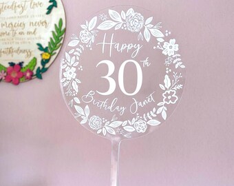 Könnte beinhalten: Weißer Acryl-Kuchentopper mit einem floralen Kranzdesign. Der Topper sagt "Happy 30th Birthday Janet".