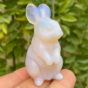 May include: A white opal rabbit figurine with iridescent details. The rabbit is sitting upright with its ears perked up.