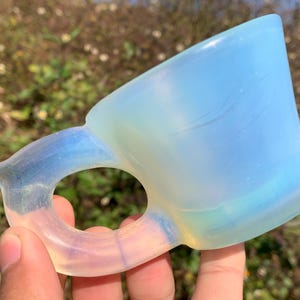 以下が含まれることがあります： 白いオパールガラスのカップで、ハンドルが付いています。カップは半透明で、わずかに青みがかっており、ハンドルはリングの形をしています。