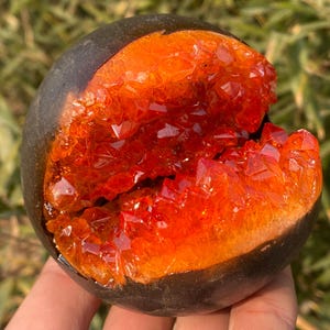 May include: A dark brown sphere with a crack revealing a bright orange crystal formation inside.