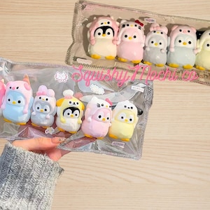 Op de afbeelding: Een set van 10 kleurrijke pinguïn-vormige squishy-speelgoed in een doorzichtige plastic zak. De speelgoedjes zijn allemaal in verschillende kleuren en hebben verschillende gezichtsuitdrukkingen. Op de zak staat "Squishy Mochi Co.".