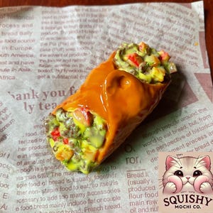 May include: A close-up of a mochi pastry with a vibrant orange glaze, filled with colorful vegetables and a creamy sauce. The pastry is on a paper with text. A cute cat logo is in the bottom right corner.