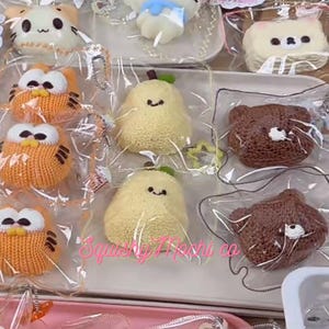 Puede incluir: Una variedad de juguetes de peluche, incluyendo búhos, osos y personajes con forma de pera, se exhiben en una bandeja. Los juguetes están empaquetados individualmente en plástico transparente. Los búhos son naranjas con detalles blancos y negros. Los osos son marrones y las peras son amarillas.