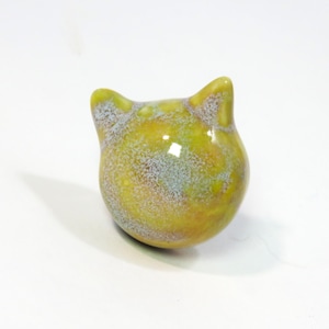 May include: A ceramic cat figurine with a yellow and green glaze. The glaze has a speckled effect with white and blue flecks.