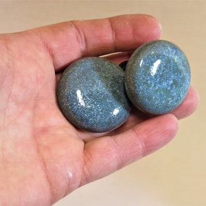 May include: Two round ceramic knobs with a speckled blue and green glaze. The knobs have a glossy finish.