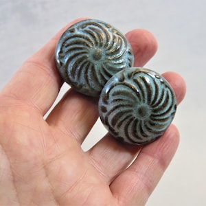 May include: Two teal blue ceramic knobs with a brown swirl design.