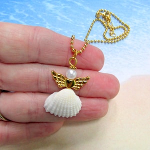 May include: A gold necklace with a seashell angel pendant. The pendant features a white seashell body, gold wings, and a pearl head. The necklace chain is gold.