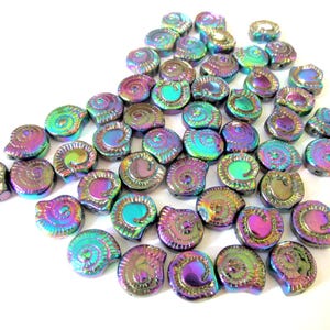 May include: A collection of small, iridescent ammonite-shaped beads featuring a metallic finish with shifting hues of purple, blue, green, and gold. Each bead displays a detailed spiral shell pattern with a smooth, reflective surface texture.