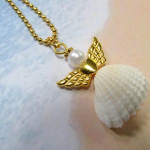 May include: A gold-coloured necklace with an angel pendant. The pendant has gold wings, a pearl, and a white seashell body. The necklace chain is made of small, gold-coloured beads.