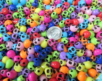 May include: A large pile of colorful plastic skull beads. The beads are in various shades of pink, purple, blue, green, yellow, orange, and red. The beads are all about the size of a dime.