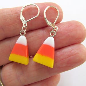 May include: Candy corn earrings with silver-colored leverback closures. Each earring features a candy corn design with white, orange, and yellow layers. These earrings are a fun accessory for Halloween or any time of year.