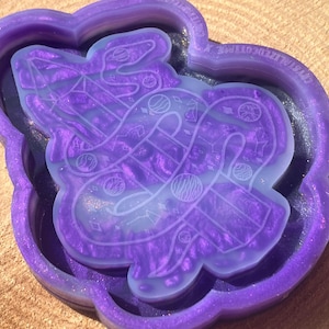 Puede incluir: Un molde de resina púrpura con un diseño de una serpiente envuelta alrededor de una varita. El molde es translúcido y tiene un acabado brillante.