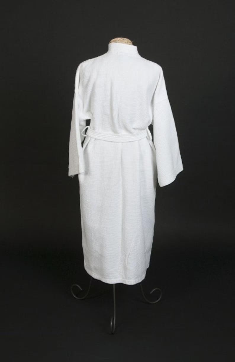 May include: A white bathrobe with a shawl collar and a tie belt. The robe is made of a soft, absorbent material and is perfect for lounging around the house.