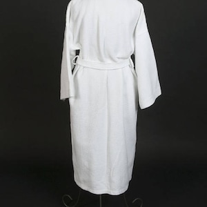 May include: A white waffle weave bathrobe with a self-tie belt. The robe is hanging on a stand against a black background.