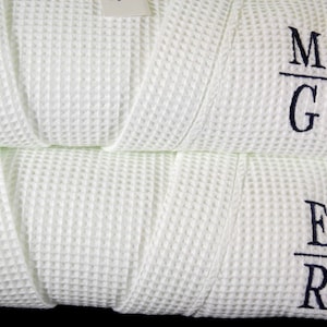 May include: Two white waffle weave robes with embroidered initials. The top robe has the initials "M/G" and the bottom robe has the initials "E/R".