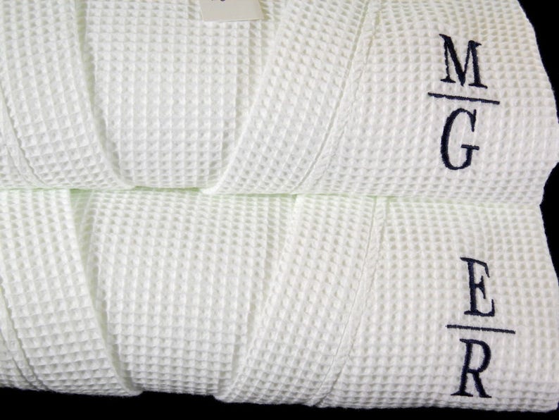 May include: Two white waffle weave robes with embroidered initials. The top robe has the initials "M/G" and the bottom robe has the initials "E/R".