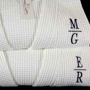 May include: Two white waffle weave robes with black embroidered initials. The top robe has the initials "M/G" and the bottom robe has the initials "E/R".