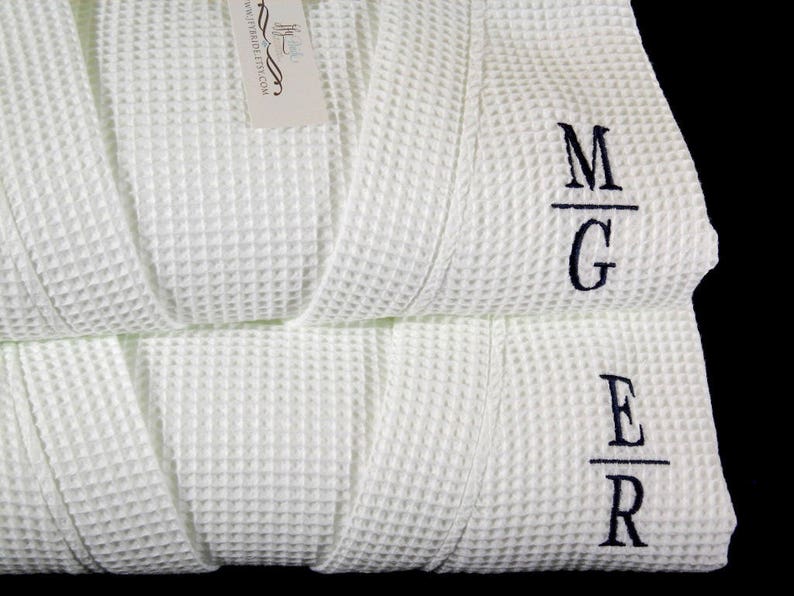 May include: Two white waffle weave robes with black embroidered initials. The top robe has the initials "M/G" and the bottom robe has the initials "E/R".