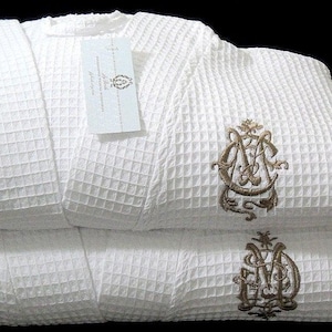 May include: White waffle weave bathrobe with a gold embroidered monogram. The robe is folded in half and the monogram is visible on both sides.