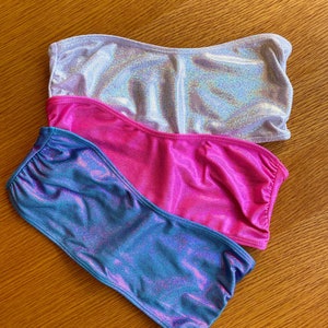 May include: Three tube tops in different colors: silver, pink, and blue. The tube tops are made of a shiny, iridescent fabric.