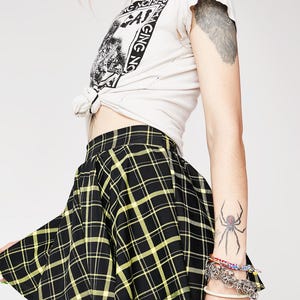 May include: Black and yellow plaid mini skirt with a pleated design. The skirt is made of a soft, lightweight fabric and has a comfortable fit.