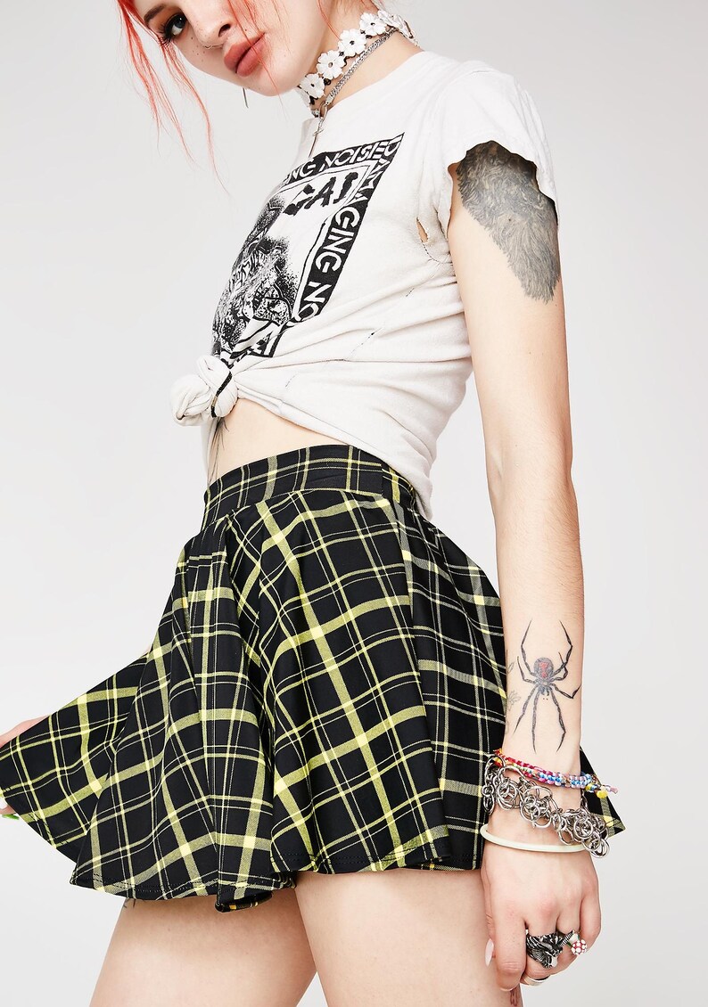 May include: Black and yellow plaid mini skirt with a pleated design. The skirt is made of a soft, lightweight fabric and has a comfortable fit.