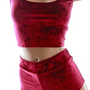 May include: A burgundy velvet two-piece outfit. The top is a crop top with a scoop neckline and wide straps. The bottoms are high-waisted shorts with a folded waistband. The fabric has a soft, textured appearance.
