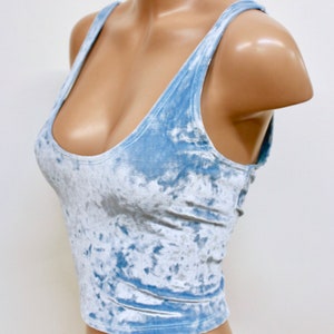 May include: A light blue cropped tank top made of crushed velvet. The tank top has a scoop neck and thin straps.