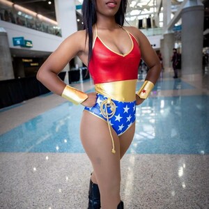 May include: A woman dressed as Wonder Woman in a red, gold and blue costume with a star-spangled design. She is wearing black boots and a gold headband.